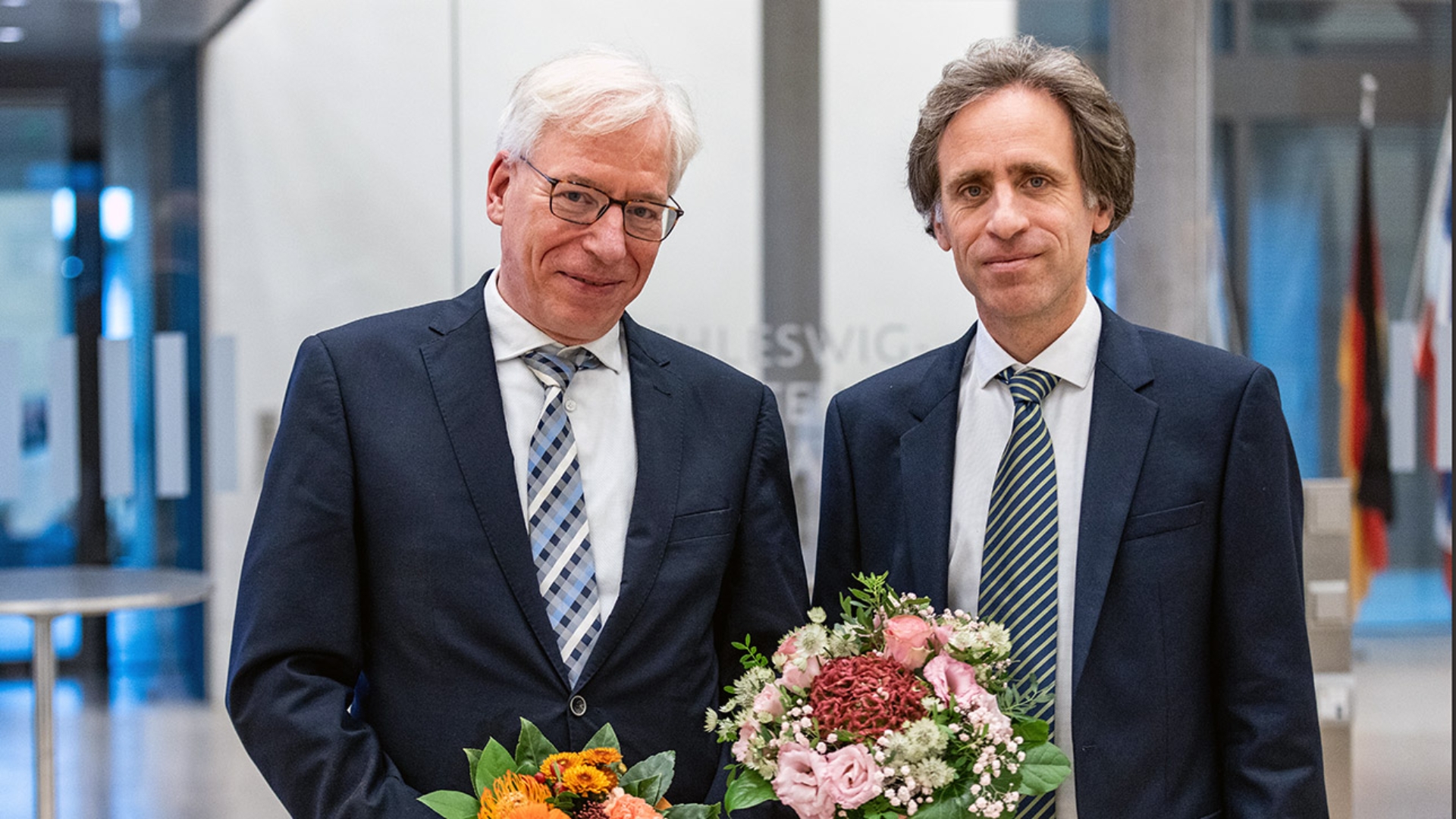Landesverfassungsgericht Richter Mitglieder Richter Carsten Löbbert Dr. Marc Petit © Foto: Landtag, Sönke Ehlers Pressefoto Carsten Löbbert und Dr. Marc Petit, die beide einen Blumenstrauss in den Händen halten.
